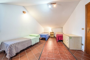 A small, well-lit attic bedroom with two beds, a dresser, and a door.