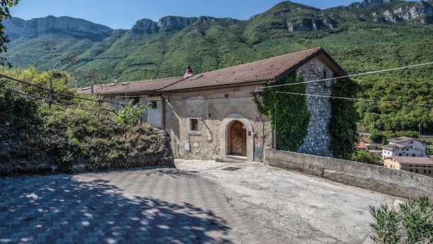 A stone building with a tiled roof, an arched entrance, and a view of green mountains in the background. - Il Sentiero del Riccio (Sicignano degli Alburni)