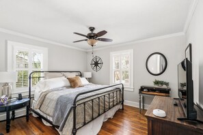 Une chambre à coucher comprenant un lit, un ventilateur de plafond, une table de chevet, une commode, un miroir et une fenêtre avec des stores.