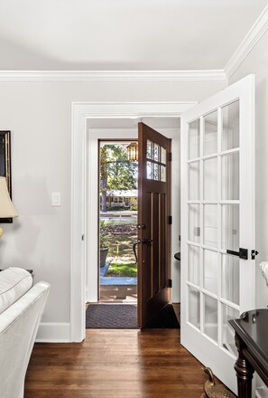 A hallway with a wooden floor leading to a door with a glass panel, a white wall, and a small outdoor area visible through the door. - The Cottage on Boundary (Aiken)