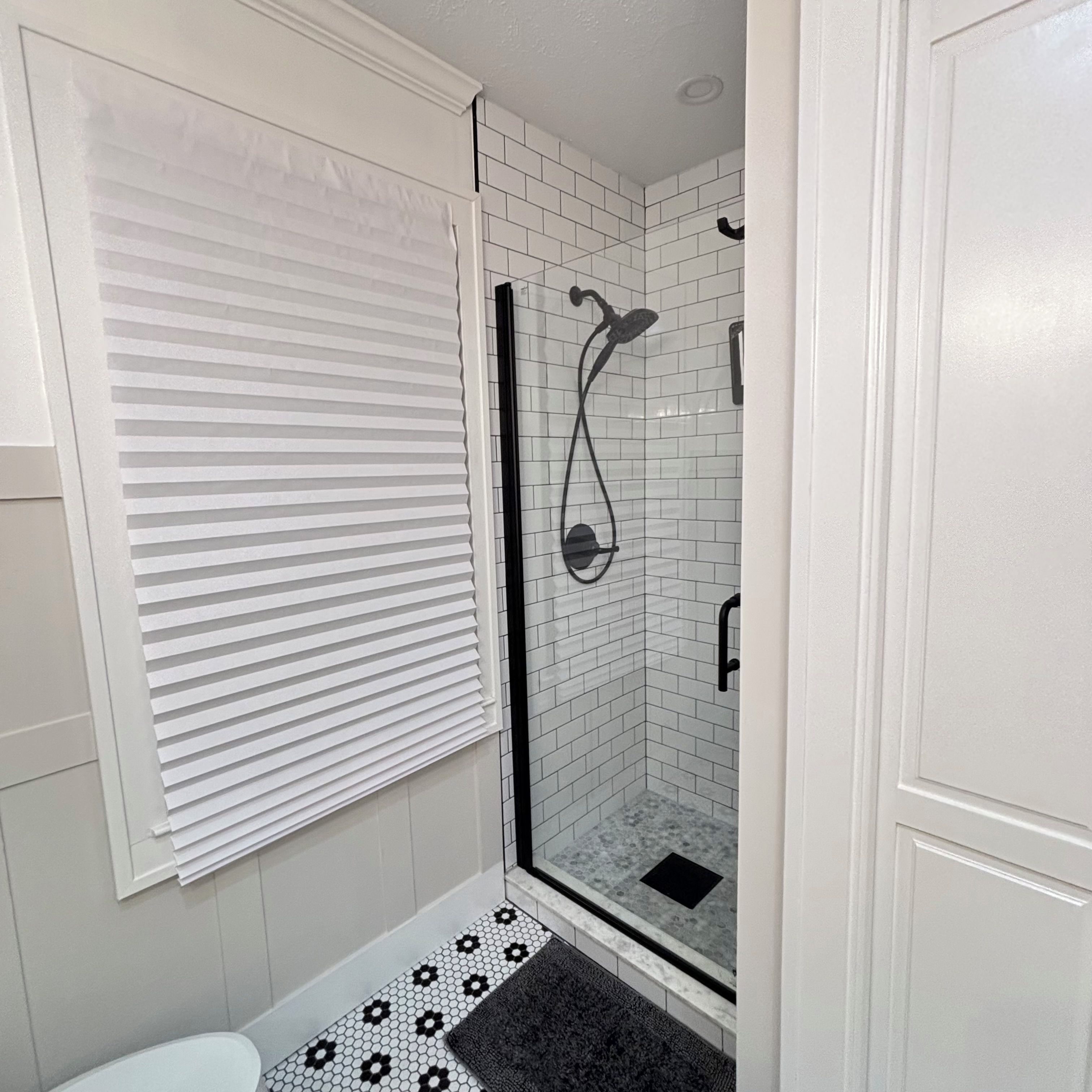 A bathroom with a shower, toilet, and a window with blinds.
