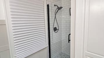 A bathroom with a shower, toilet, and a window with blinds.