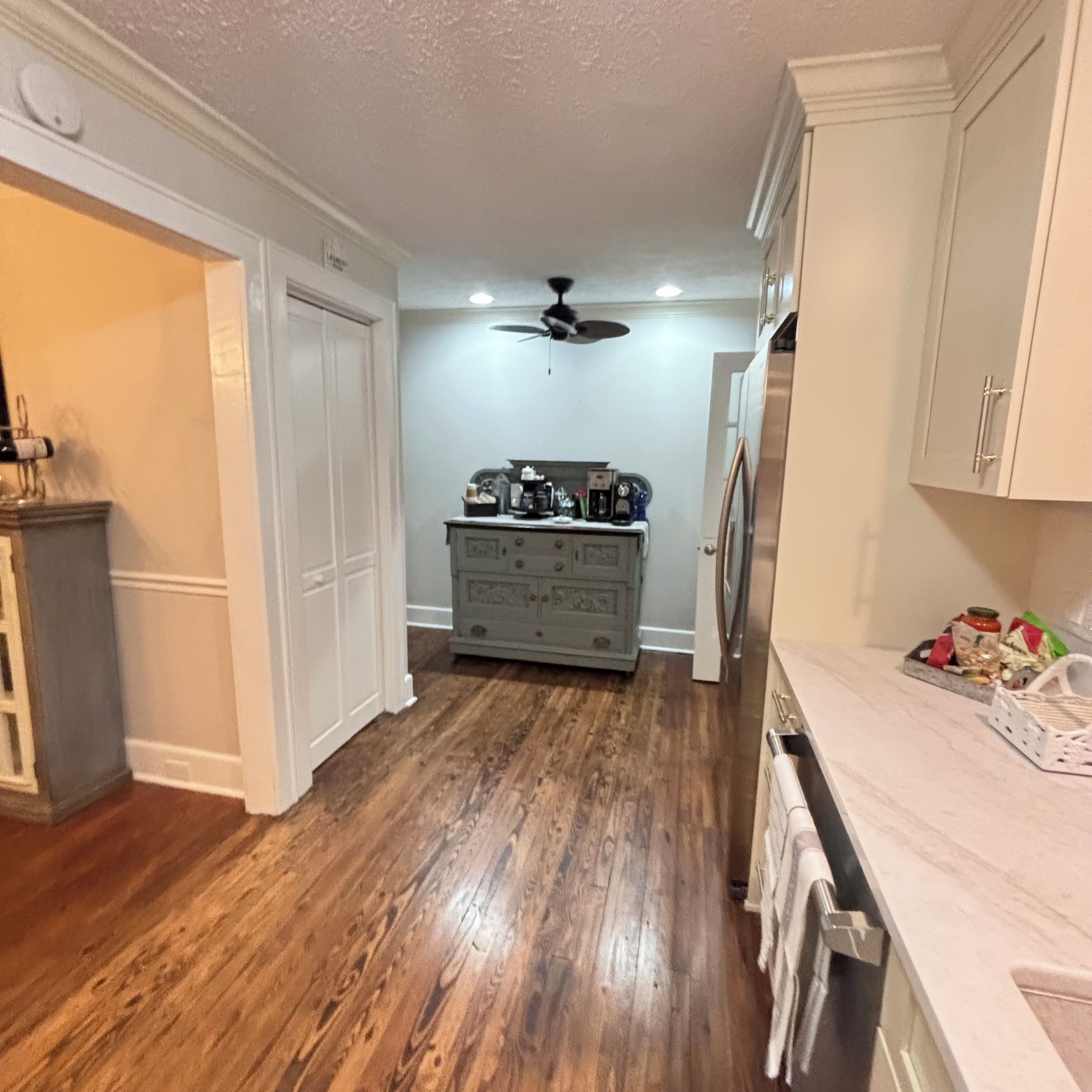 A kitchen with wooden flooring, white cabinetry, and a ceiling fan.