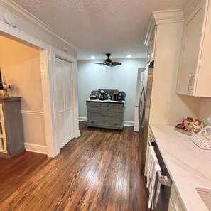 A kitchen with wooden flooring, white cabinetry, and a ceiling fan.