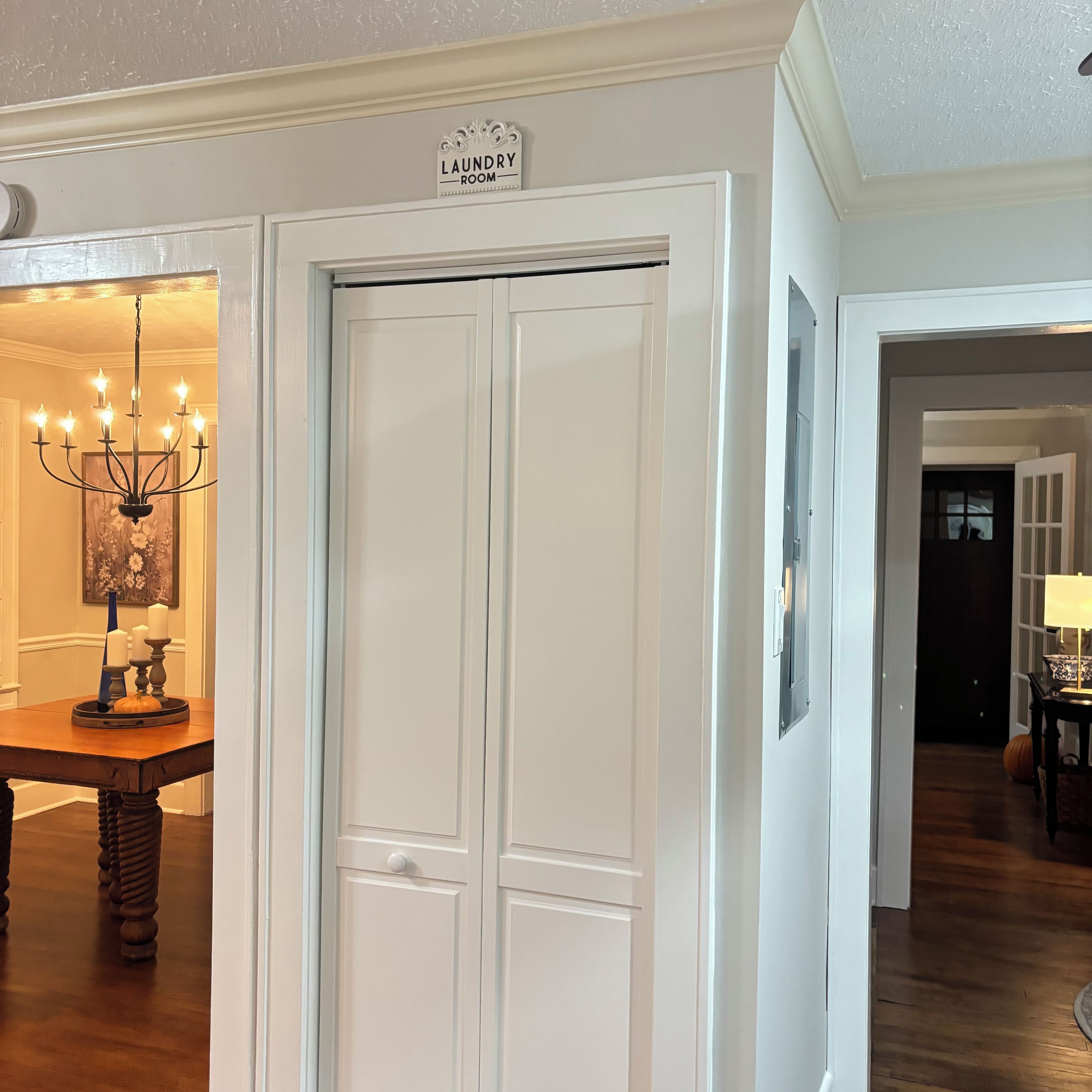 A hallway with a closed door labeled 'Laundry Room,' a chandelier, a table with a pumpkin decoration, and a lamp.