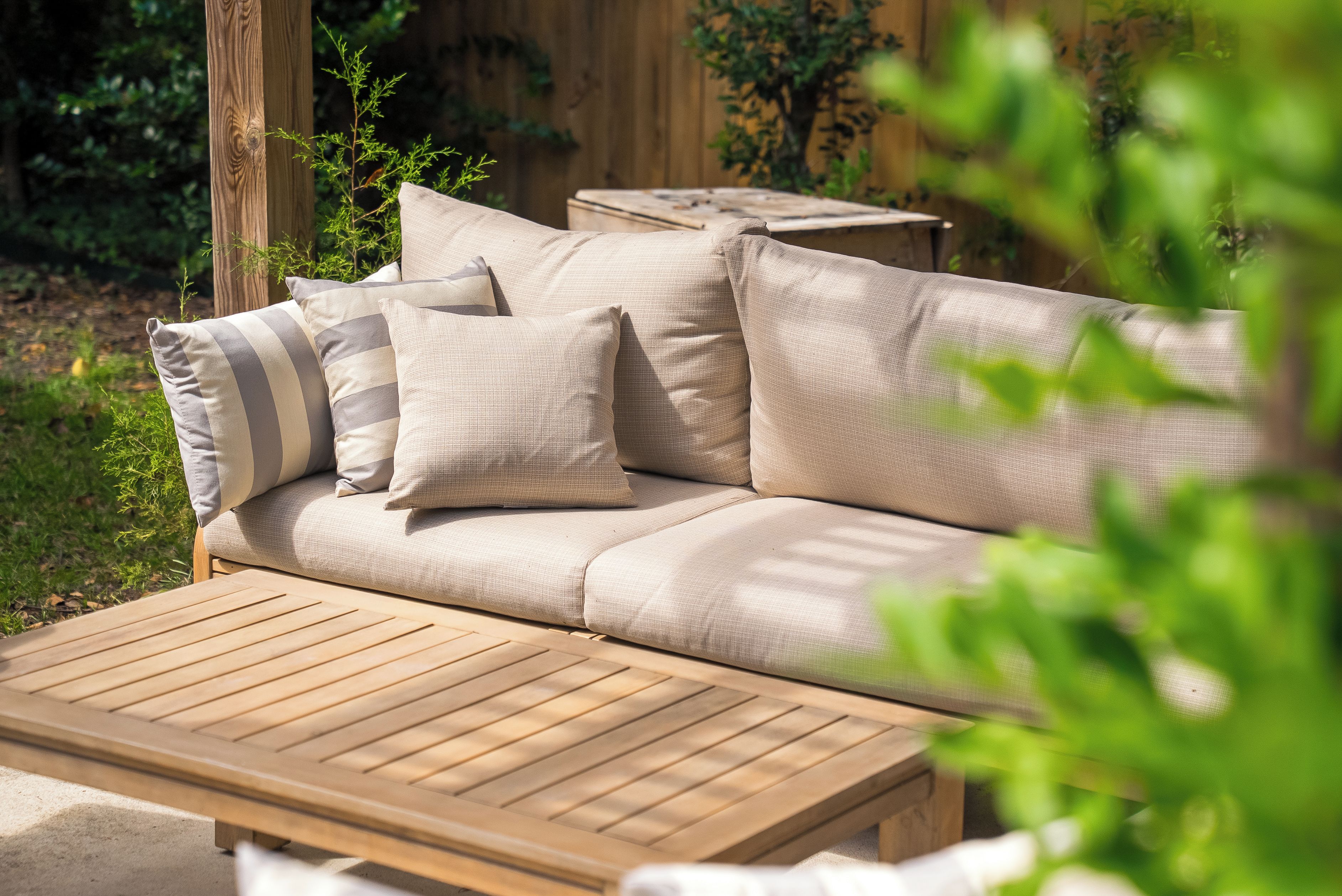 Un espacio de estar exterior de madera con un sofá y cojines beige.