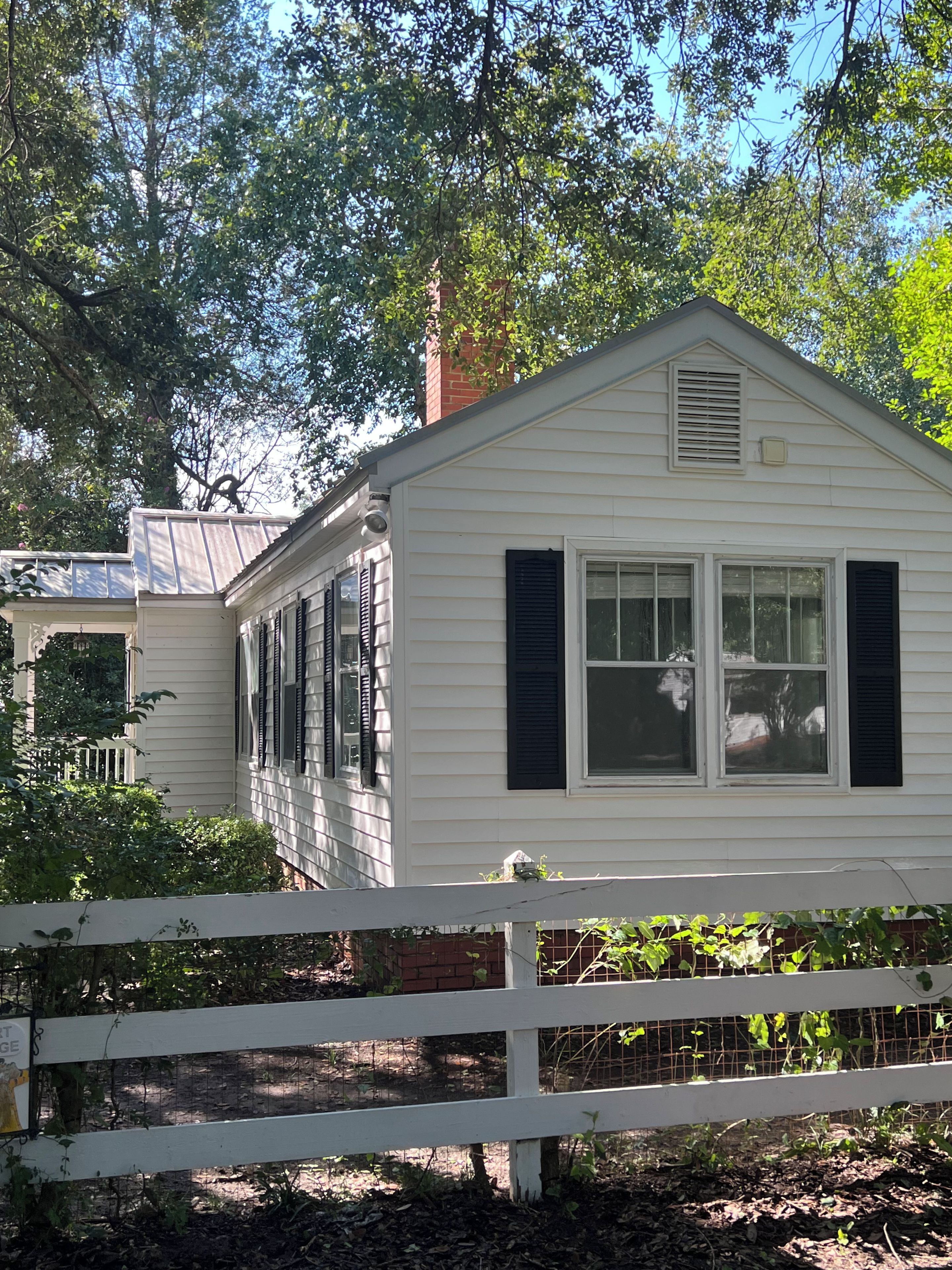A white single-story house with dark shutters, a visible chimney, and a white picket fence.