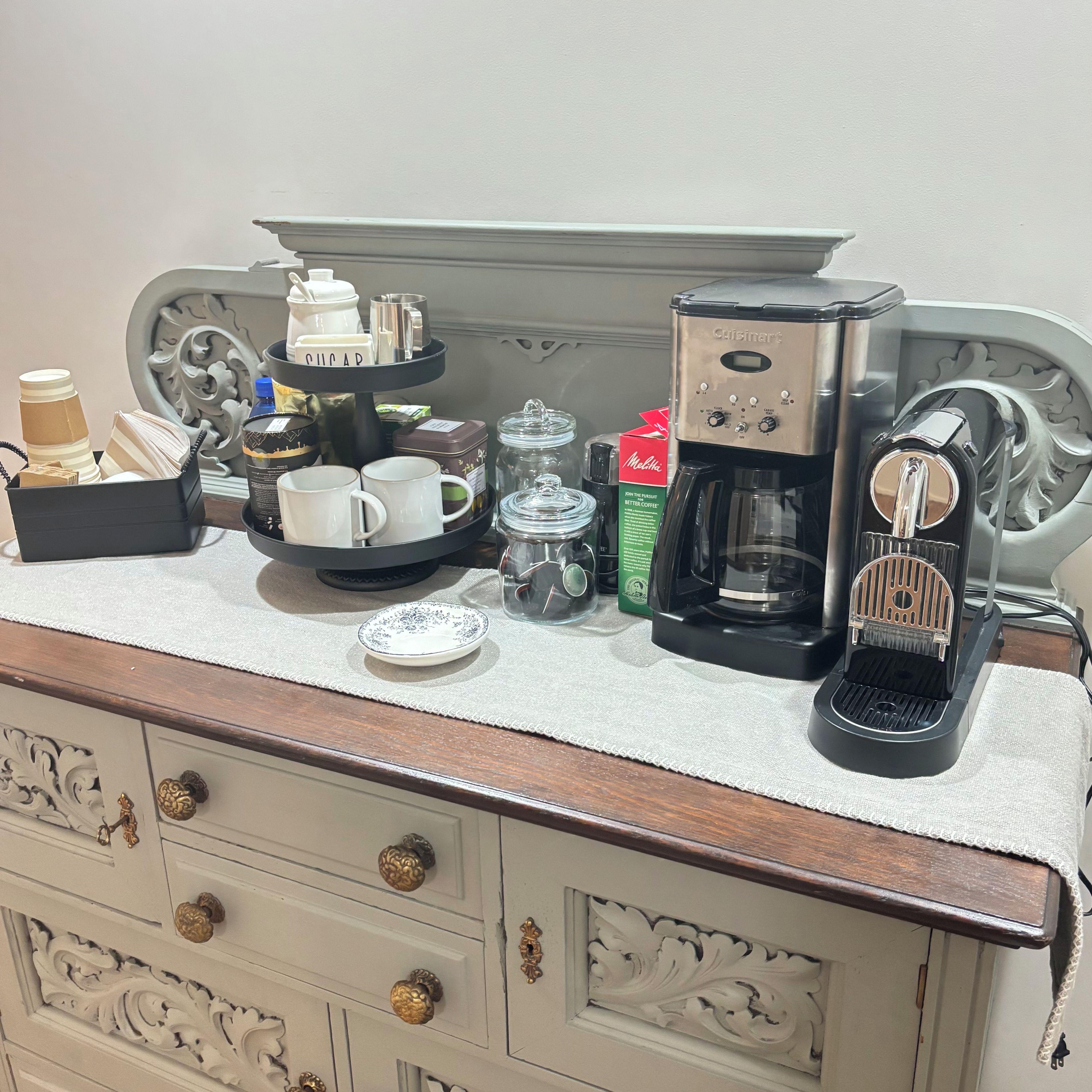 Una kitchenette equipada con cafetera, tazas, jarra de café y una bandeja con azúcar y leche condensada.