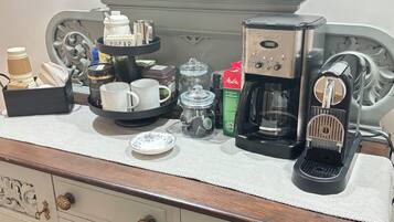 Una kitchenette equipada con cafetera, tazas, jarra de café y una bandeja con azúcar y leche condensada.