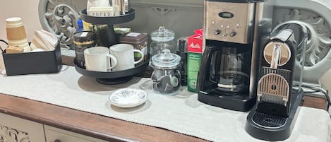 A kitchenette with a coffee maker, mugs, a coffee pot, and a tray with sugar and creamers.