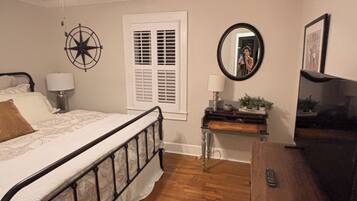Un dormitorio con cama, escritorio, espejo, ventilador de techo y ventana con persianas.