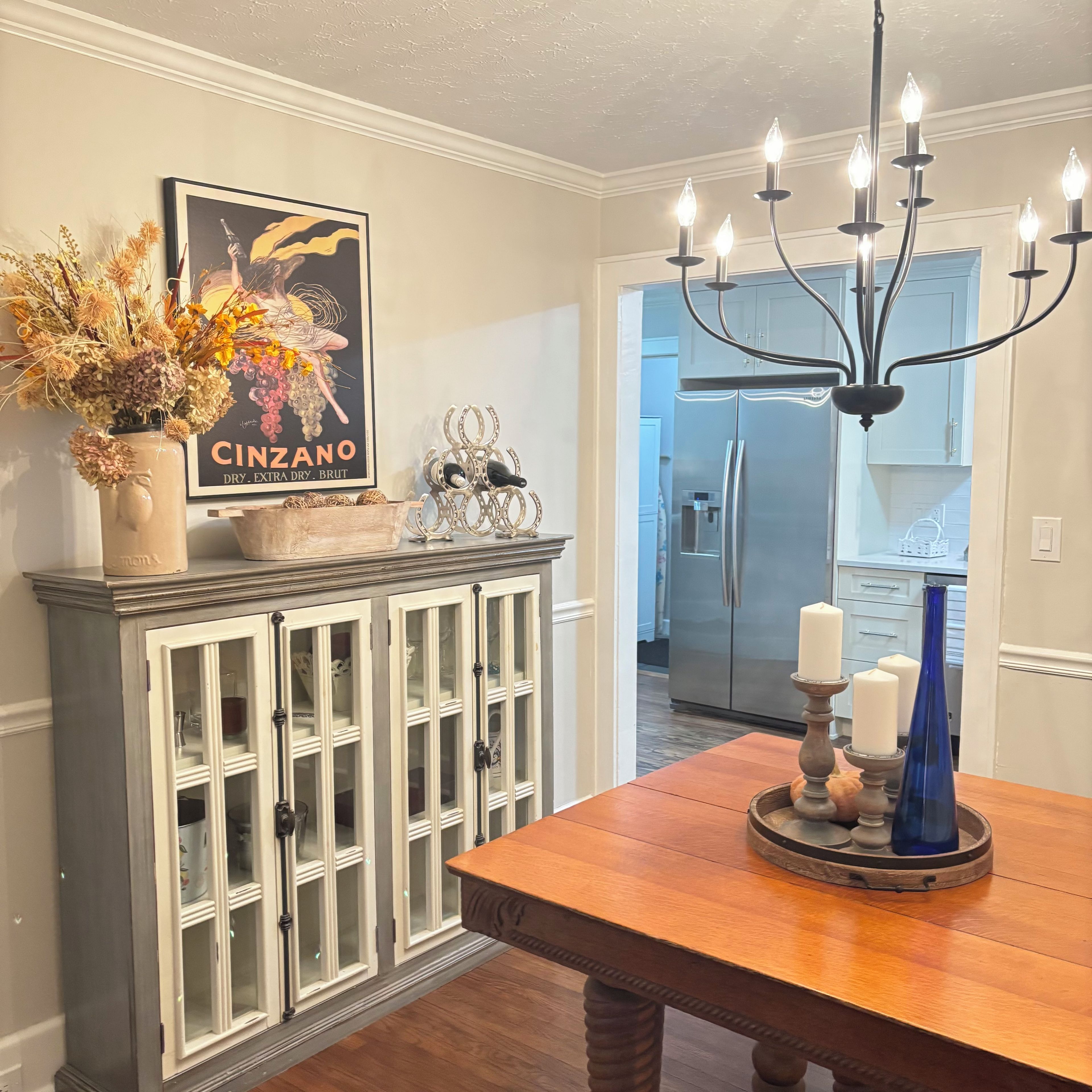 A dining area with a wooden table, a chandelier, a cabinet with glass doors, and a poster on the wall.