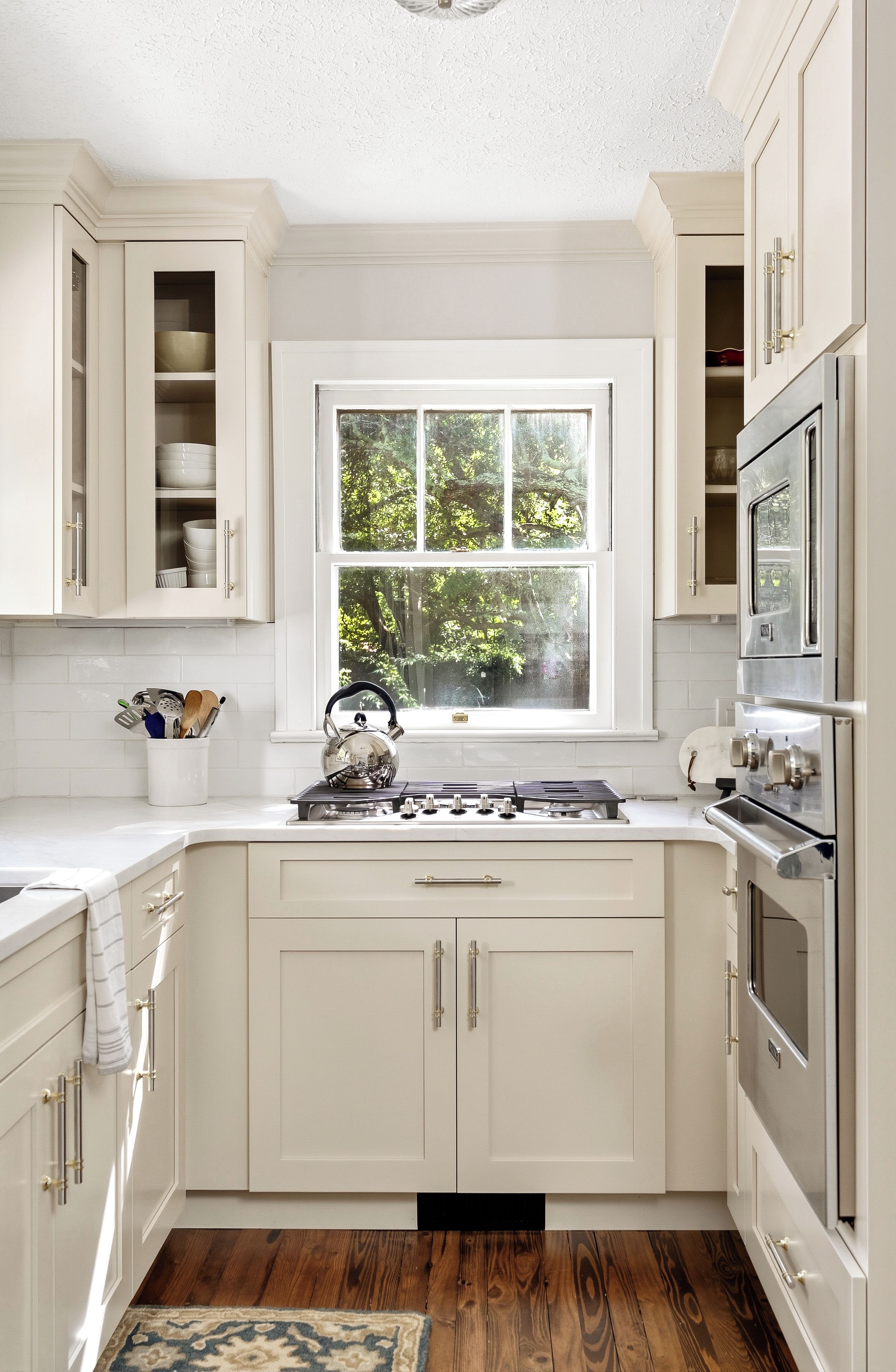A kitchen with white cabinetry, a window with a view of trees, a kettle on the stove, and stainless steel appliances.