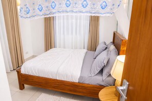 Un dormitori amb llit de fusta, cortines beix i un dosser blanc amb dibuixos blaus.