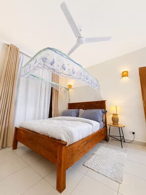 A bedroom with a wooden bed, a ceiling fan, a bedside lamp, and a small table with a lamp. - Quaint 1-bedroom apartment in Ukunda perfect for relaxing stays (Ukunda)