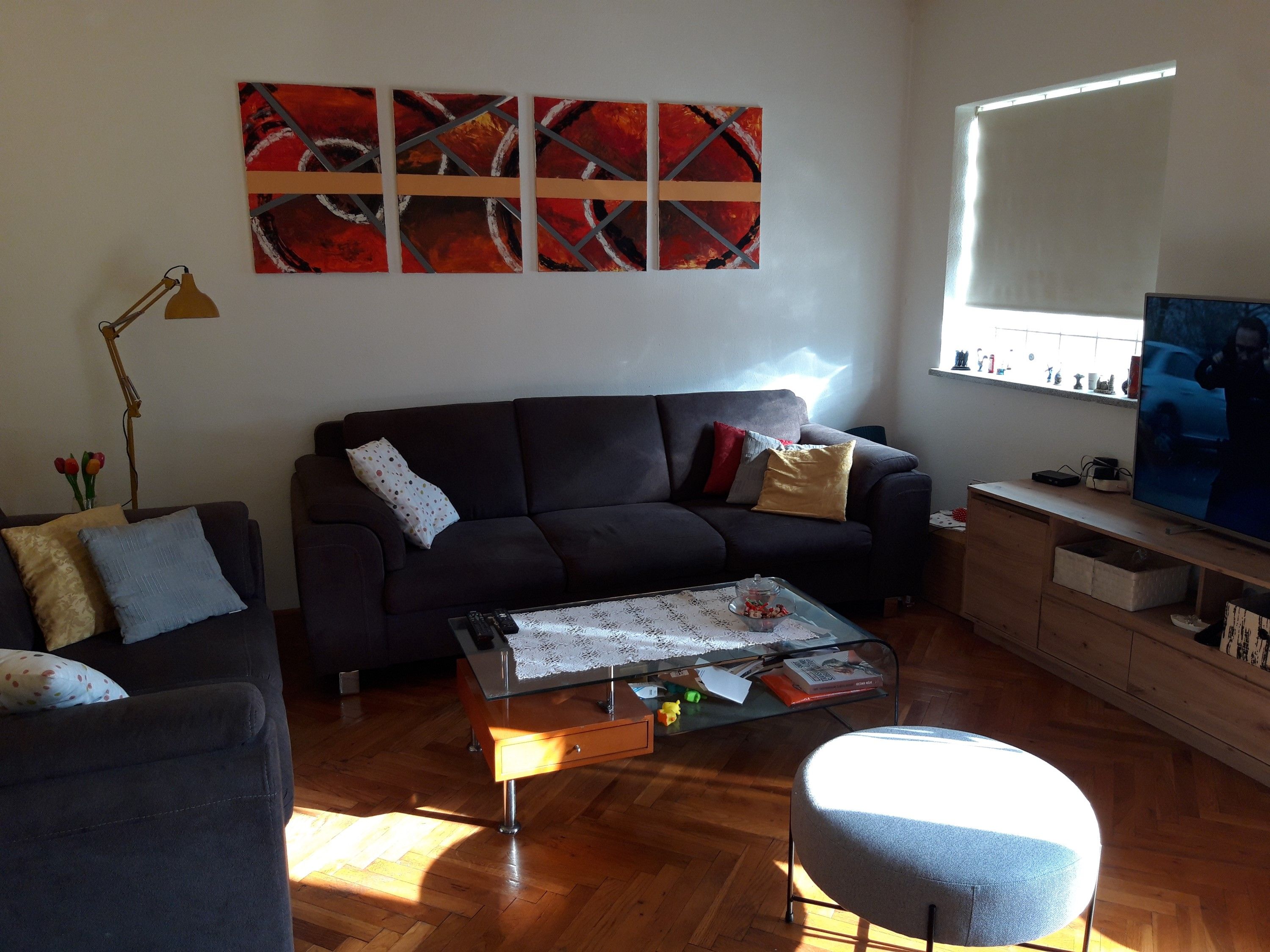 A living room with a dark sofa, a glass coffee table, and a large abstract painting on the wall.