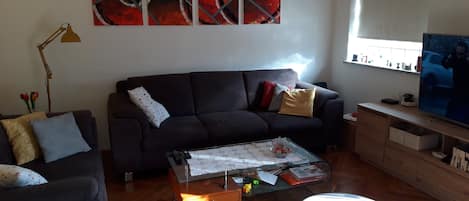 A living room with a dark sofa, a glass coffee table, and a large abstract painting on the wall.