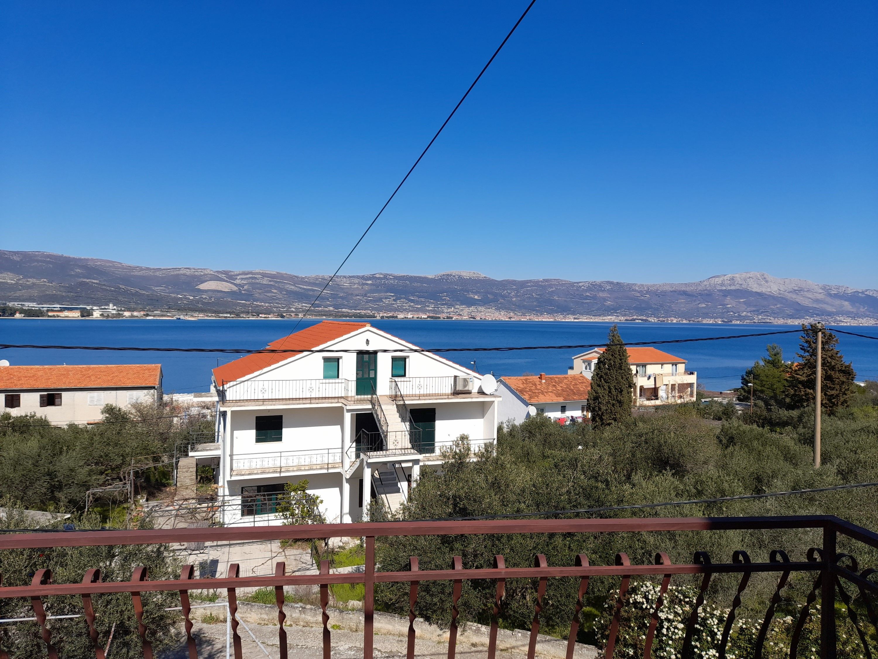 Un bâtiment blanc avec un toit rouge, un balcon et une vue sur la mer et les montagnes en arrière-plan.
