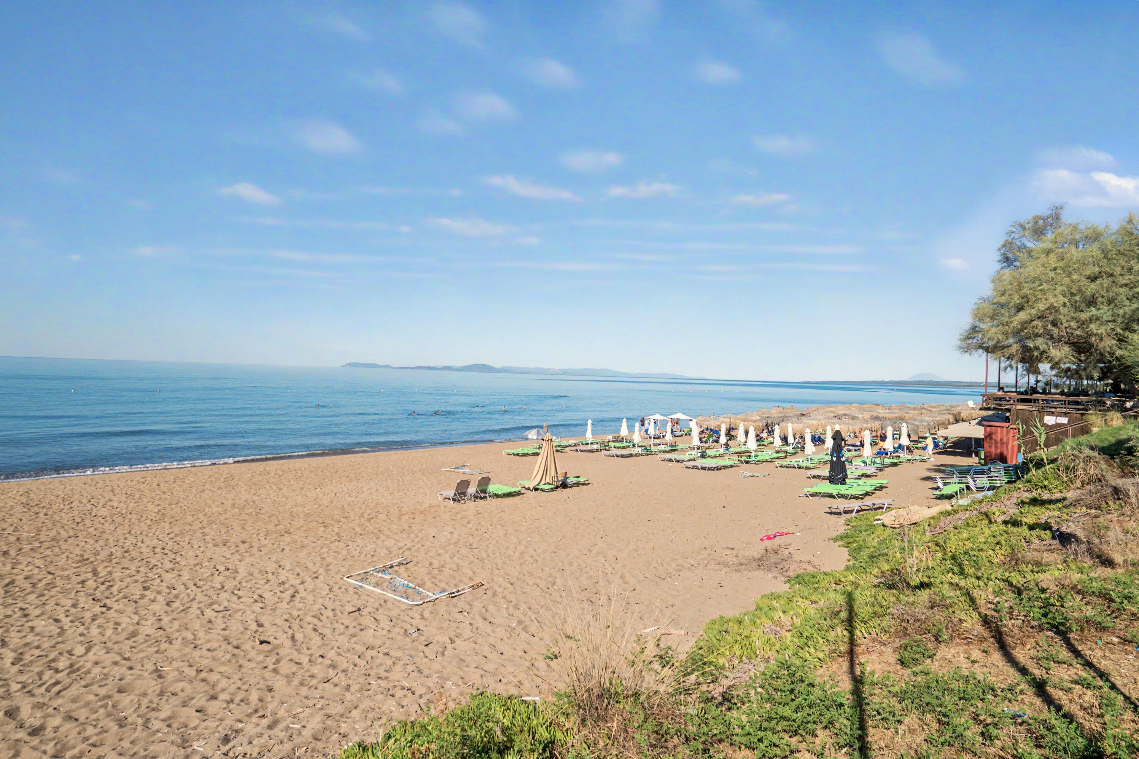 A beach with sun loungers and umbrellas, a clear sky, and a calm sea.