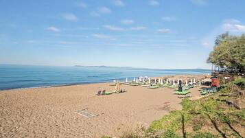 A beach with sun loungers and umbrellas, a clear sky, and a calm sea.