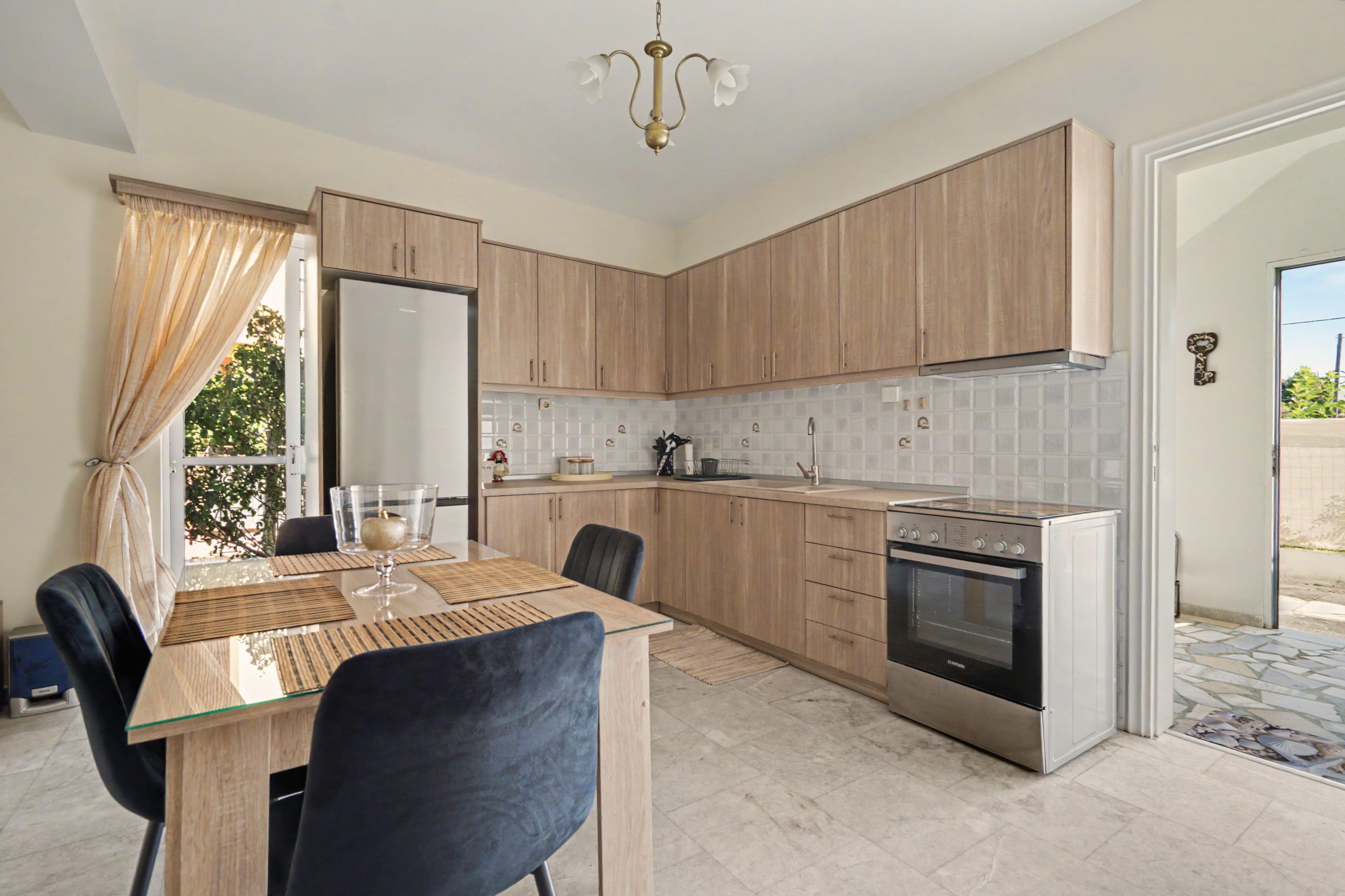 A modern kitchen with wooden cabinets, a stainless steel refrigerator, an oven, and a dining area with a glass table and chairs.