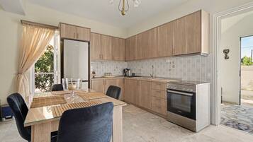 A modern kitchen with wooden cabinets, a stainless steel refrigerator, an oven, and a dining area with a glass table and chairs.