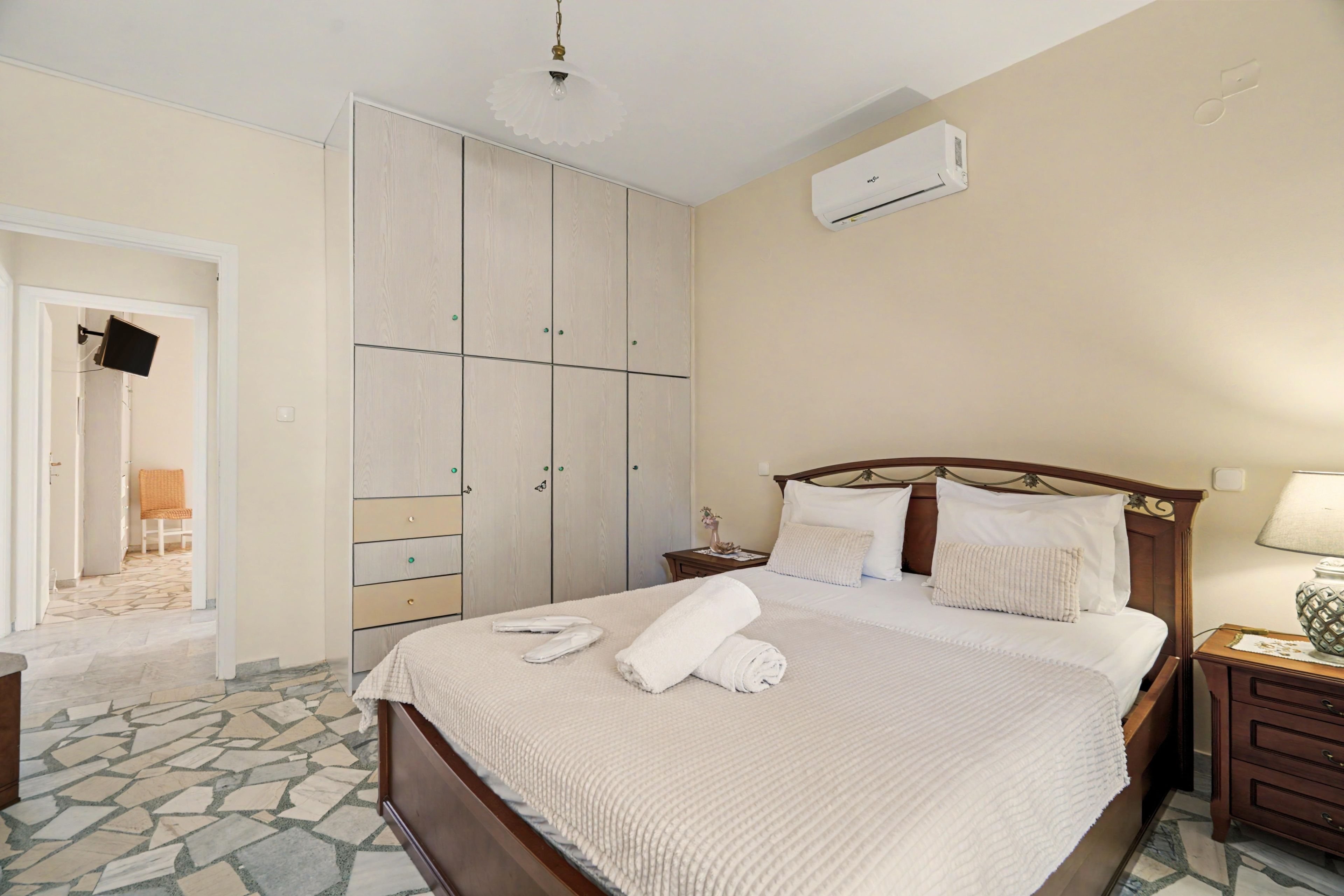A hotel room with a bed, a nightstand, a bedside table, a wardrobe, and an air conditioning unit.