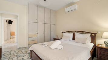 A hotel room with a bed, a nightstand, a bedside table, a wardrobe, and an air conditioning unit.