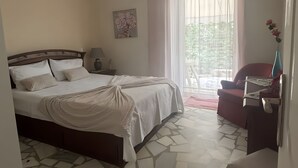 Ein Schlafzimmer mit einem Bett, einem Nachttisch, einer Lampe, einem Gemälde, einem Fenster mit Vorhängen und einem roten Sessel.