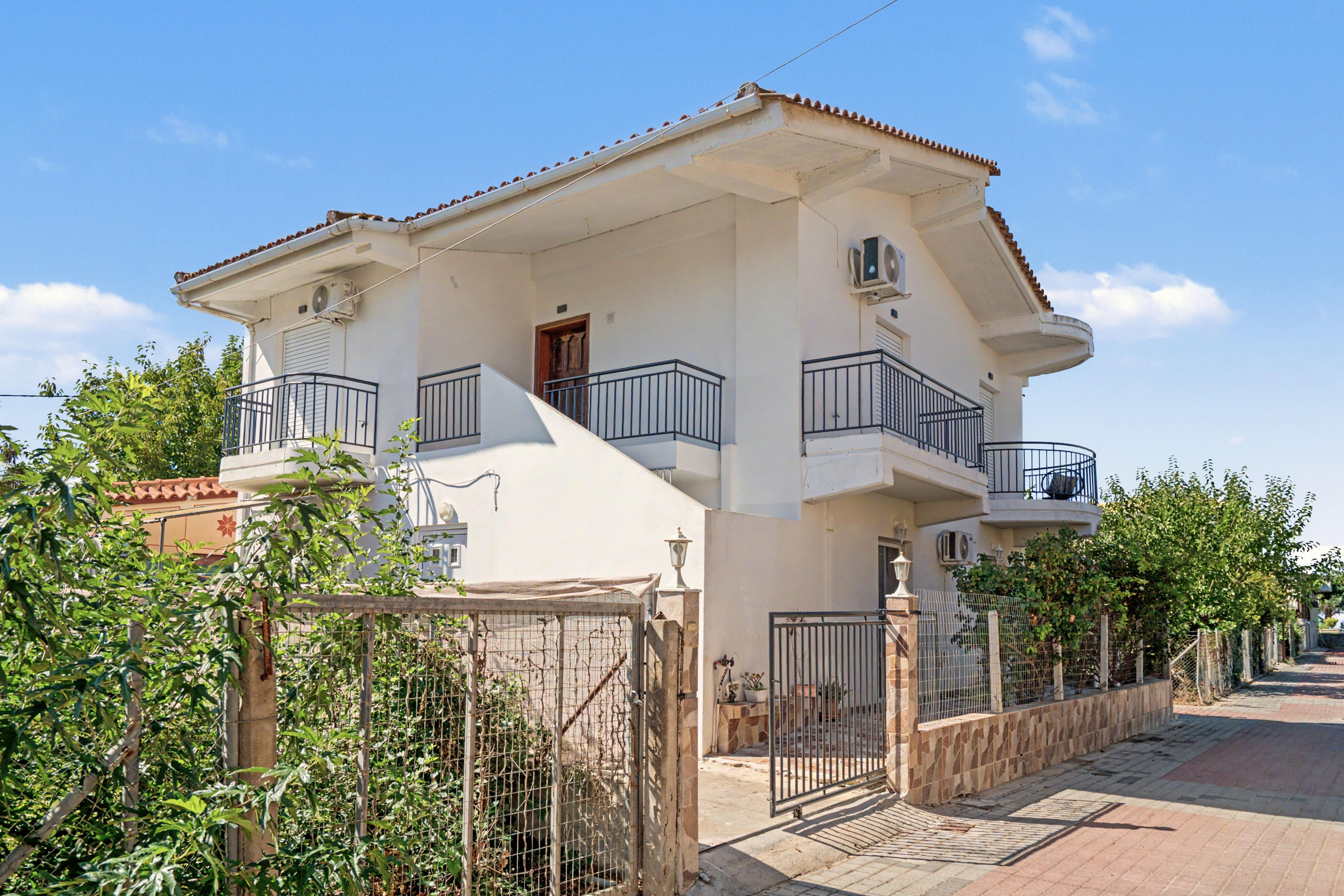 A two-story residential building with a balcony, a gate, and a paved driveway.