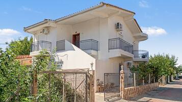 A two-story residential building with a balcony, a gate, and a paved driveway.
