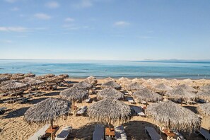A beach with thatched umbrellas and sun loungers.