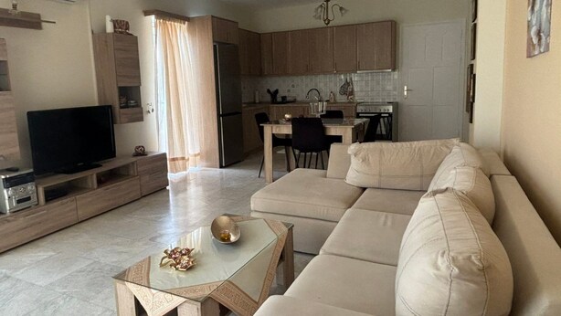 Ein Wohnzimmer mit einem beigen Sofa, einem Glastisch und einem Flachbildfernseher.
