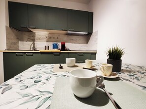 Una cocina con armarios verde oscuro, un salpicadero de mármol y una mesa con mantel floreado.