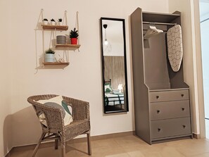 Una habitación con una silla de mimbre, un armario gris, un estante con plantas y un cuadro enmarcado.