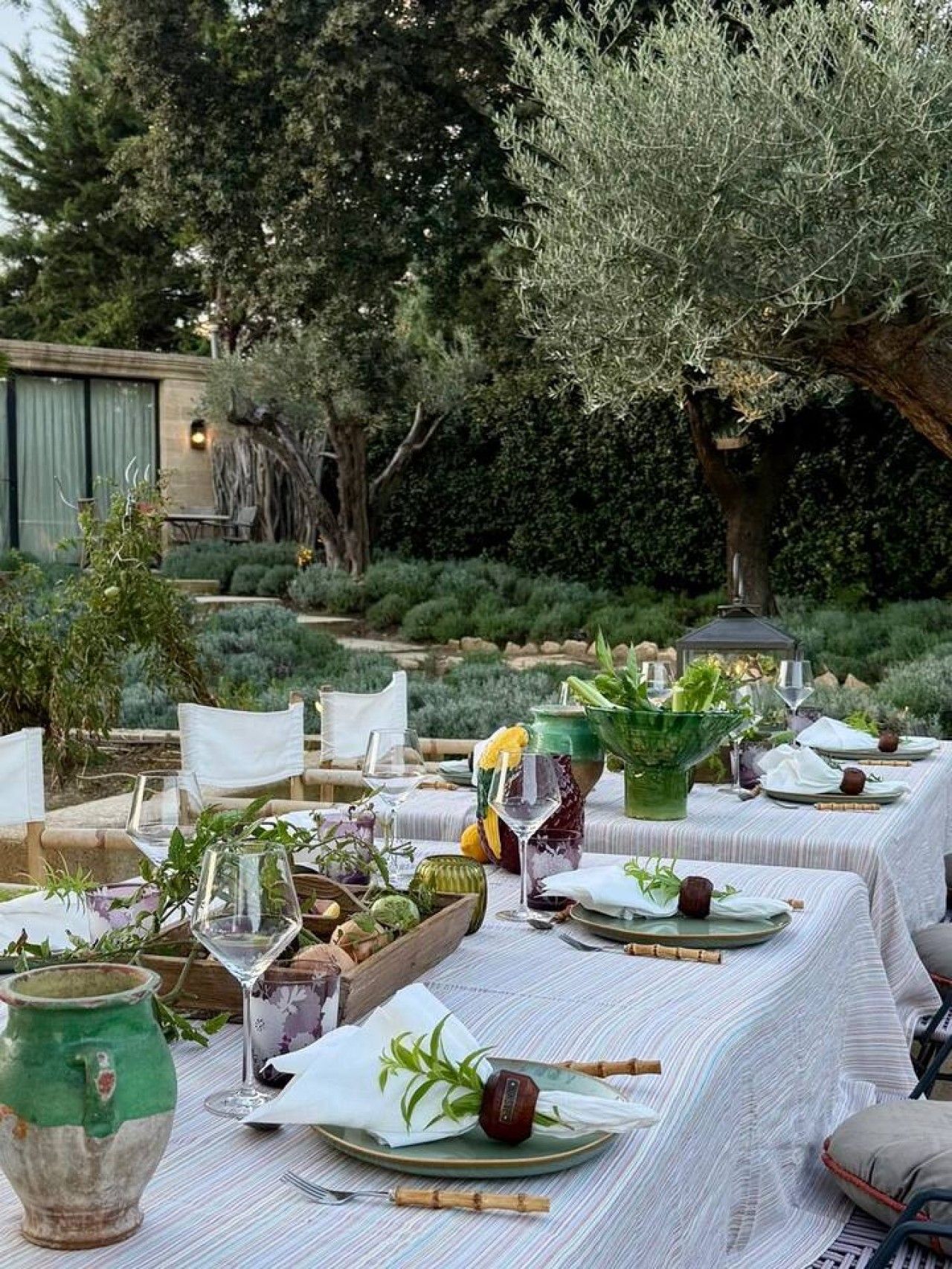 An outdoor dining area with tables set for a meal, surrounded by greenery and trees.