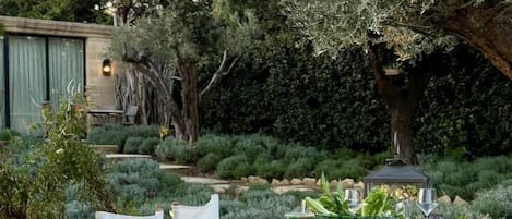 An outdoor dining area with tables set for a meal, surrounded by greenery and trees.