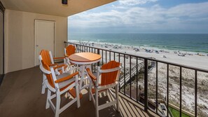 A balcony with a view of a beach, featuring a table and chairs. - Phoenix I 1052 2 Bedroom Condo (Orange Beach)