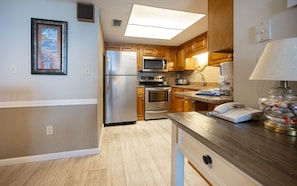 A kitchen with stainless steel appliances, wooden cabinets, and a countertop with a phone and decorative items. - Phoenix I 1065 2 Bedroom Condo (Orange Beach)