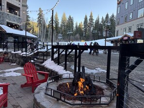 A stone building with a wooden deck, a fire pit, and red Adirondack chairs. - Indian Hills Charming Townhome 3 Bedroom Townhouse (Truckee)