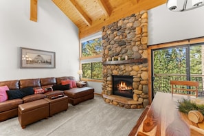 A cozy living room with a stone fireplace, leather sofa, and a dining table with a view of trees. - Indian Hills Charming Townhome 3 Bedroom Townhouse (Truckee)