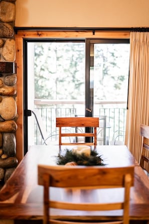 A dining table with a wooden chair in front of a stone wall and a window with a view of trees. - Indian Hills Charming Townhome 3 Bedroom Townhouse (Truckee)