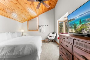 A bedroom with a bed, a ceiling fan, a TV on a dresser, a chair, and a window with a scenic view. - Indian Hills Charming Townhome 3 Bedroom Townhouse (Truckee)