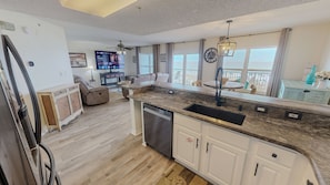 Eine moderne Küche mit integriertem Geschirrspüler, ein Essbereich mit rundem Tisch und ein Wohnzimmer mit Sofa und Fernseher.