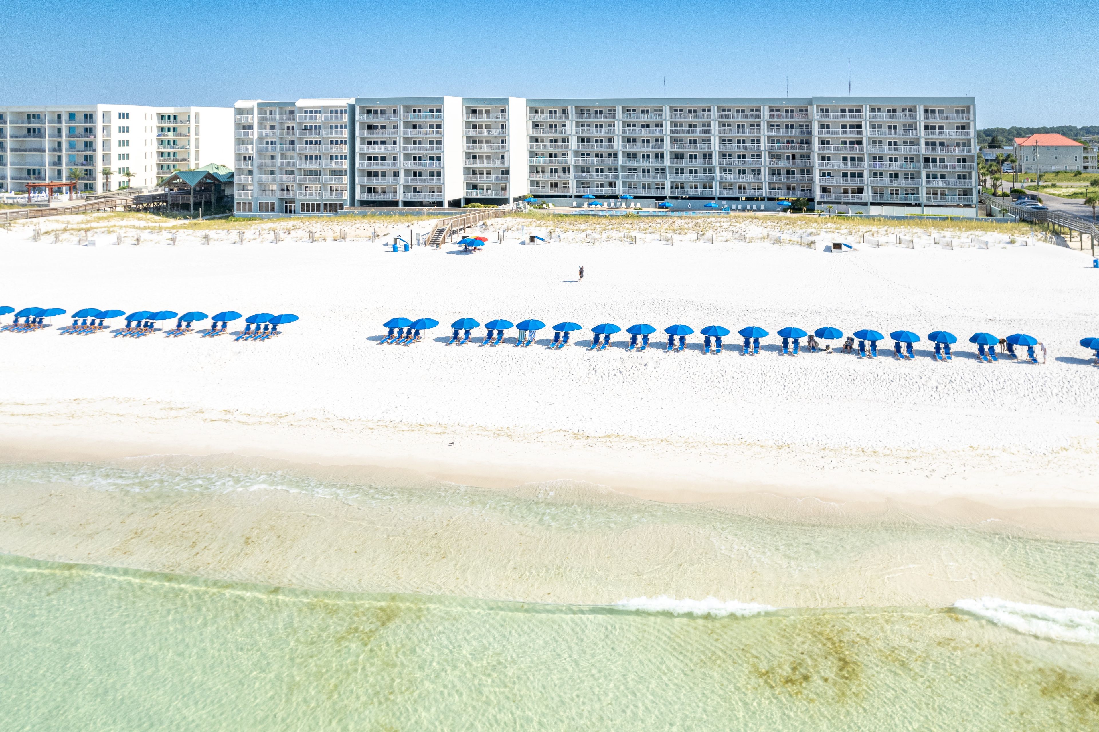 Ein Strandhotel mit mehreren Balkonen, einem Sandstrand und Sonnenschirmen.