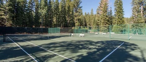 Una cancha de tenis al aire libre rodeada de árboles altos.