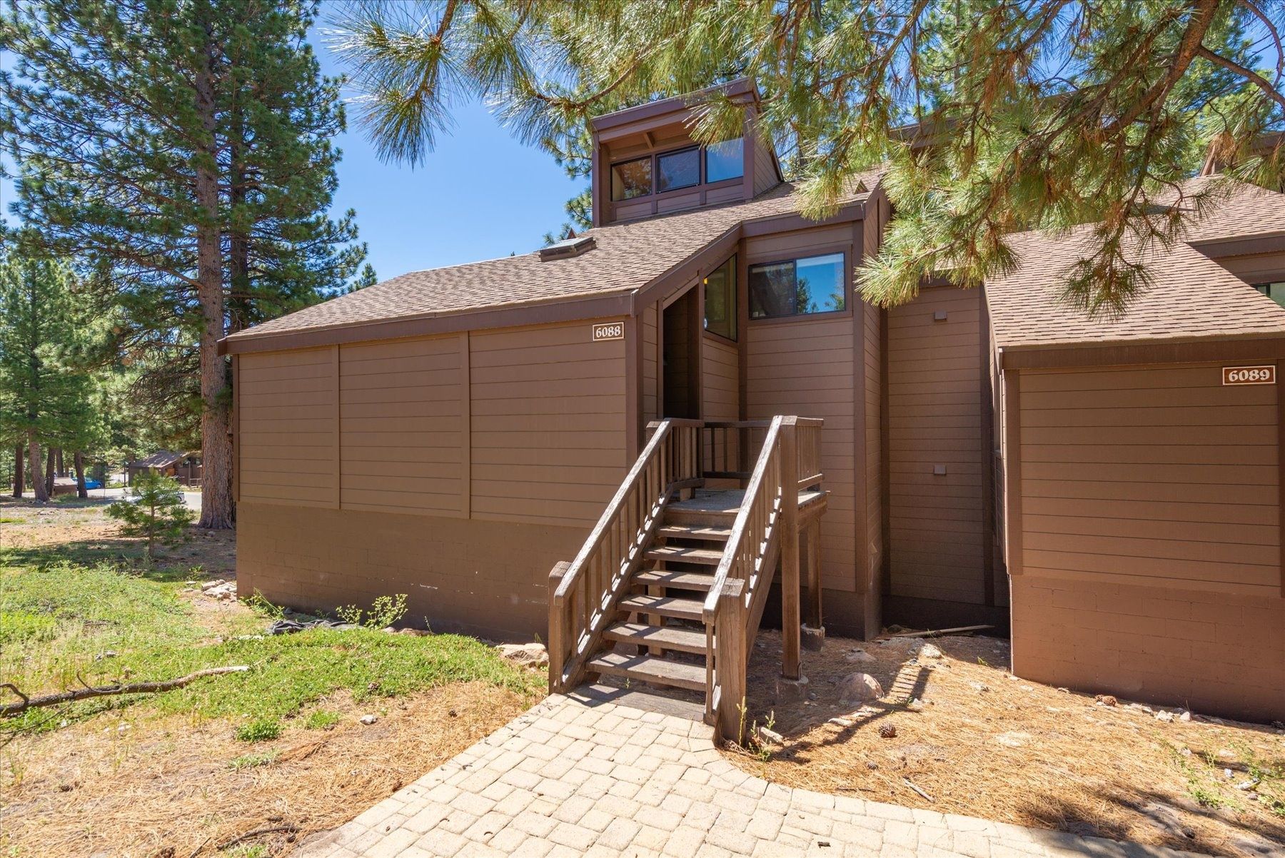 A two-story building with a wooden staircase leading to a door, surrounded by pine trees.