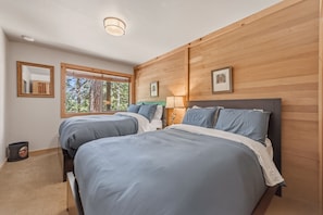 Een slaapkamer met twee bedden, een nachtkastje, een lamp en een raam met uitzicht op bomen.