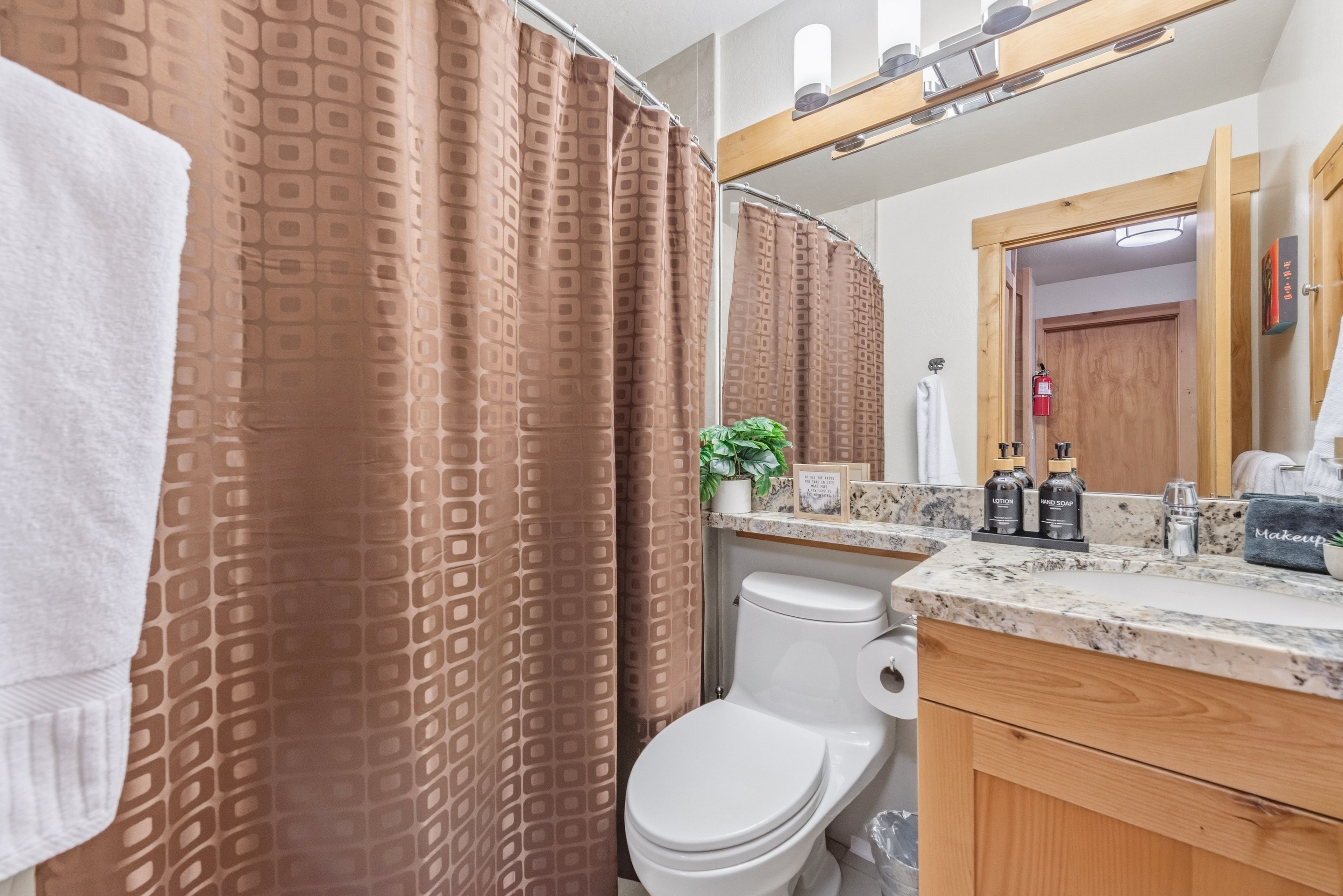 A bathroom with a shower curtain, toilet, sink with toiletries, and a mirror.
