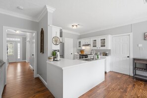 A modern kitchen with white cabinetry, a large island, and a wooden floor. - Country Living Near Lake Houston - Starry Skies 3 Bedroom Home (Dayton)